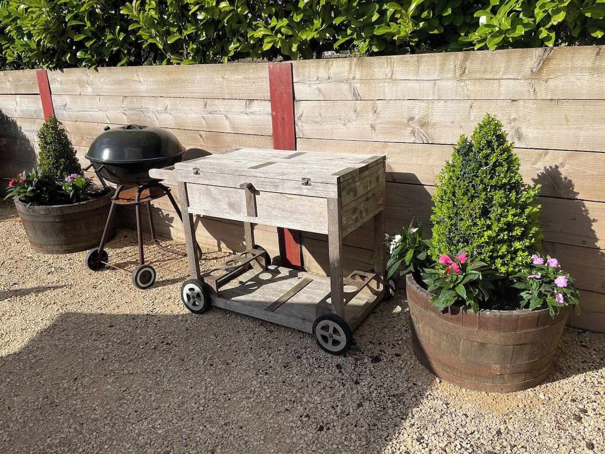 Un carret de fusta amb rodes, una barbacoa i plantes en testos.