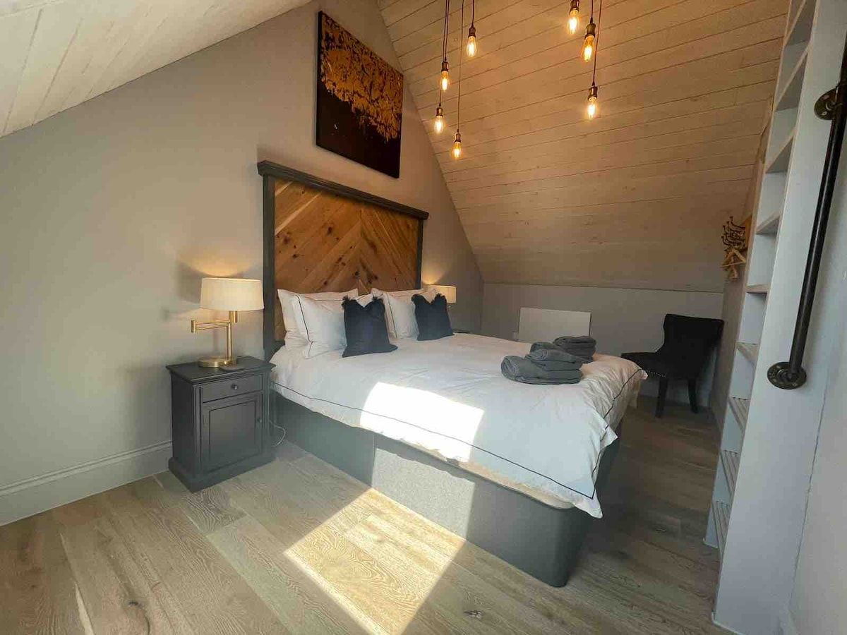 Un dormitorio con cama, mesitas de noche, cabecera y lámpara en el techo.