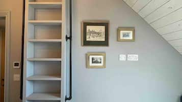 Una habitación con una escalera de madera que sube a una zona de altillo, una cama y dos cuadros en la pared.