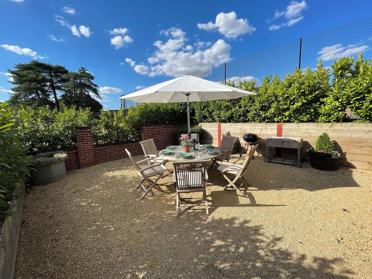 An outdoor patio with a round table and chairs, surrounded by a gravel area, under a white umbrella.