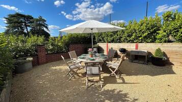 An outdoor patio with a round table and chairs, surrounded by a gravel area, under a white umbrella.