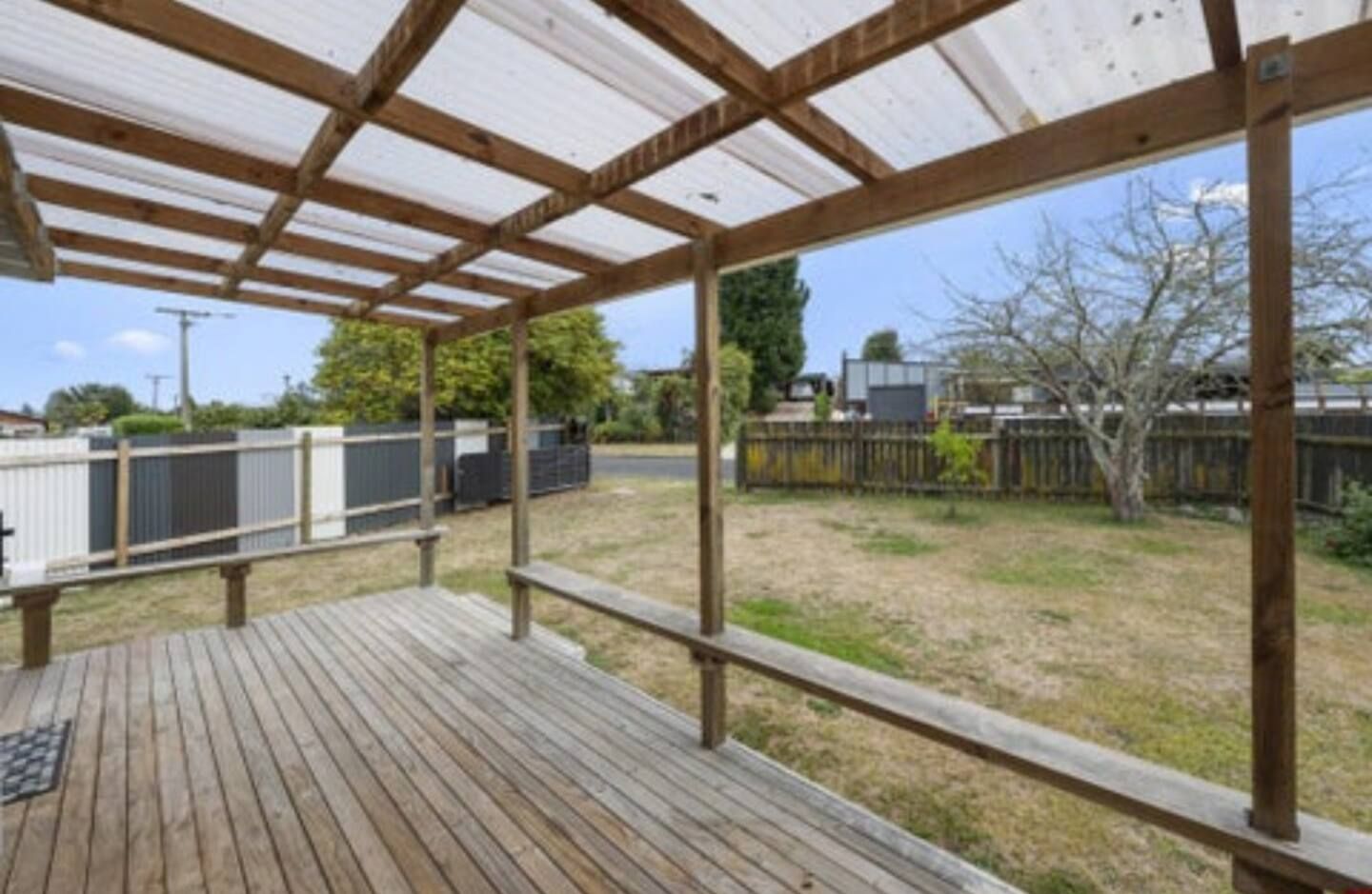 Uma área externa coberta com deck de madeira e vista para um quintal cercado.