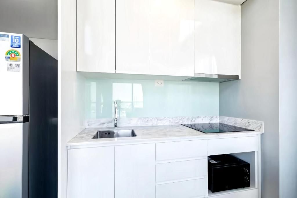 A modern kitchen with white cabinetry, a stainless steel refrigerator, a marble countertop, and a black dishwasher.