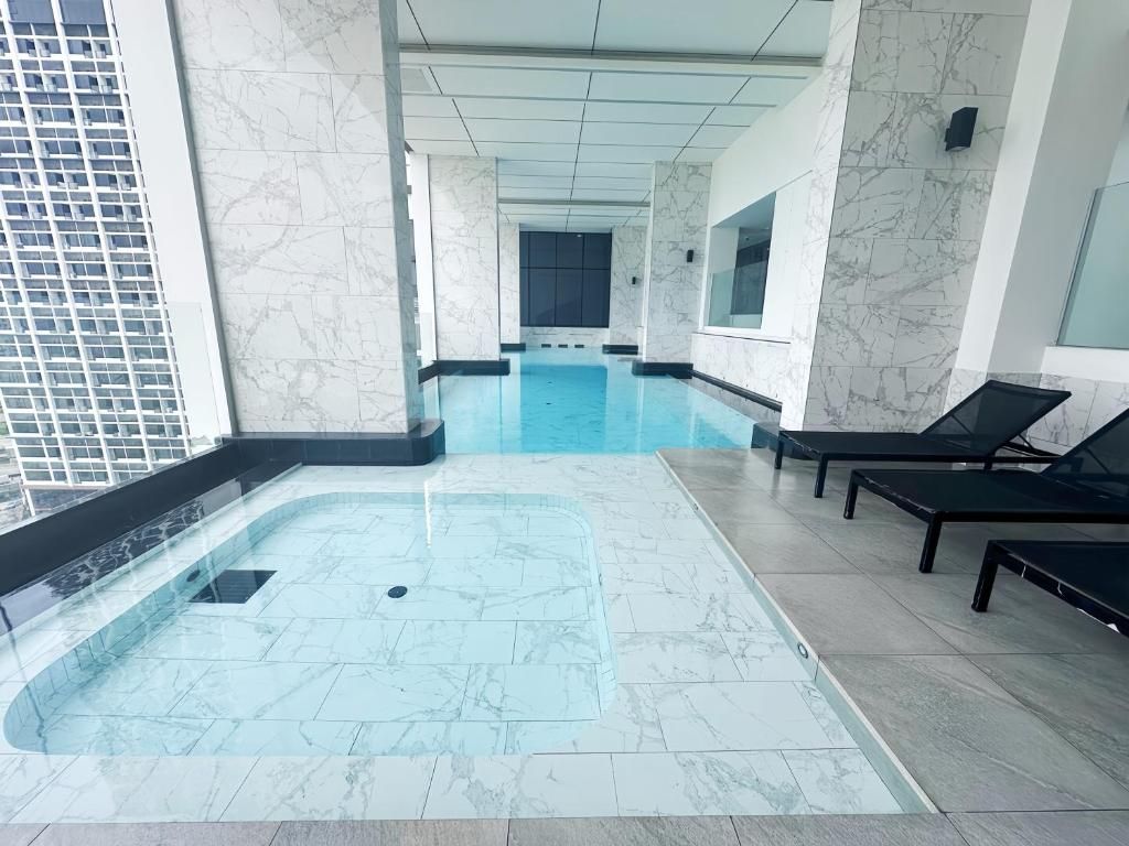 An indoor swimming pool with a marble floor and walls, surrounded by lounge chairs and a glass partition.