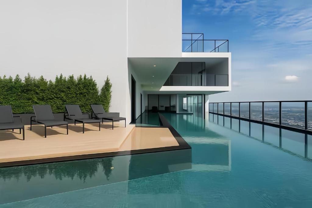 A modern infinity pool with a clear view of the city skyline, a second-floor balcony with a glass railing, and a row of lounge chairs.