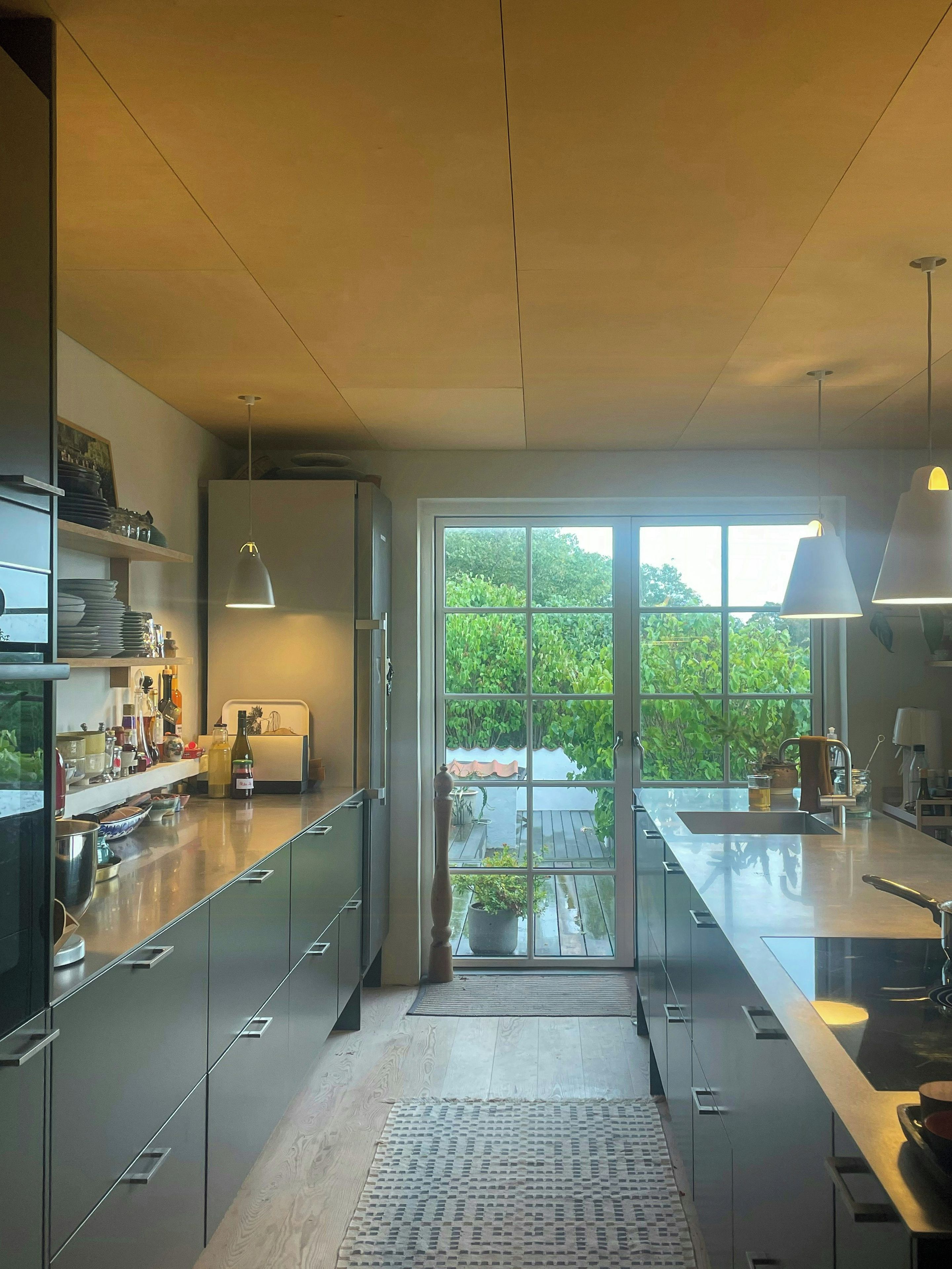 A modern kitchen with a large window, a built-in oven, and a variety of kitchenware on shelves.