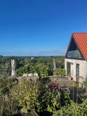 Ein modernes Haus mit rotem Dach, einer Terrasse mit Gartenmöbeln und Blick auf die Landschaft.
