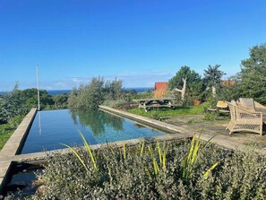 Ein rechteckiger Swimmingpool mit freiem Blick auf den Ozean, umgeben von Grünflächen und einem Picknicktisch.