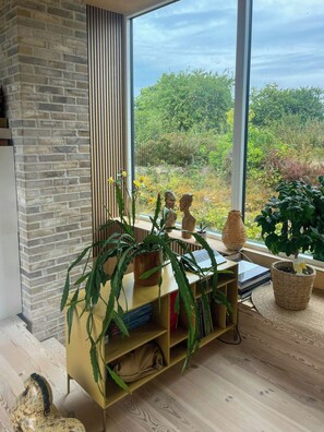 Ein Zimmer mit Backsteinwand, einem großen Fenster mit Blick auf Grünflächen, einem Holztisch mit einem Laptop und einem Bücherregal.
