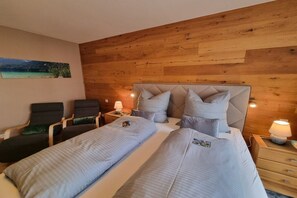 A hotel room with a wooden wall, two beds, a nightstand, a chair, and a painting. - Zugspitze 112 including sauna (Garmisch-Partenkirchen)