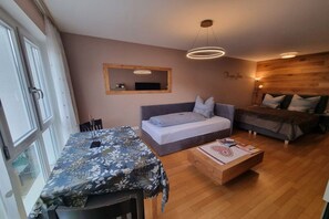 A cozy room with a bed, a sofa, a dining table, and a wooden floor. - Zugspitze 112 including sauna (Garmisch-Partenkirchen)