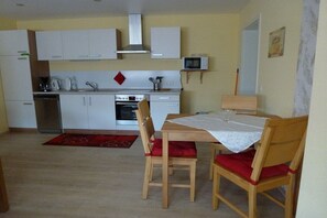 A compact kitchen with white cabinets, a microwave, and a dining area with two wooden chairs and a table. - Holiday apartment with 1 bedroom (Treis-Karden)