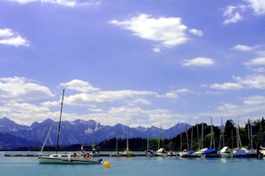 Uma marina com barcos atracados, céu claro e montanhas ao fundo.