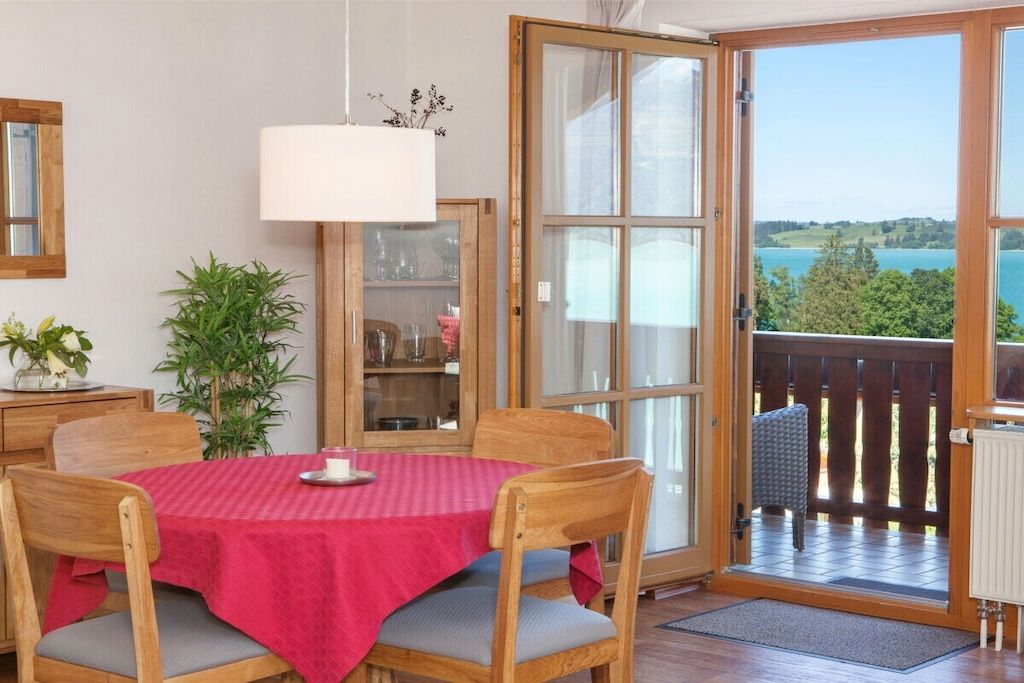 A dining area with a table set for two, a potted plant, and a view through a glass door to an outdoor deck.