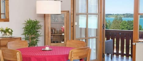 A dining area with a table set for two, a potted plant, and a view through a glass door to an outdoor deck.