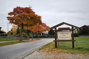 A sign indicating 'Gruss Gott in Österreichen' with a traditional wooden structure and a paved road in the background. - Holiday apartment with 1 bedroom (Rieden am Forggensee)