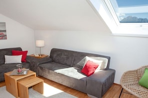 A modern living room with a grey sofa, a wooden coffee table, and a wicker chair. - Holiday apartment with 1 bedroom (Rieden am Forggensee)
