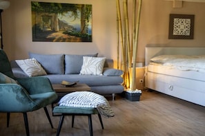 Ein modernes Schlafzimmer mit grauem Sofa, einem Bett, einem kleinen Tisch und einer Wanddekoration.