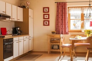 A compact kitchen with white cabinets, a wooden table, and a red and white checkered curtain. - Holiday apartment with 2 bedrooms (Halblech)