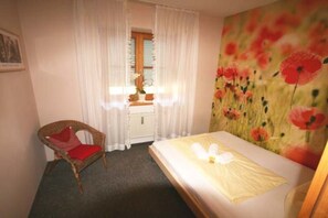 A hotel room with a bed, a chair, a window with curtains, and a wall with a floral painting. - Holiday apartment with 2 bedrooms (Halblech)