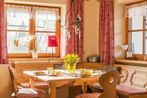 A cozy dining area with a wooden table and bench, a vase of flowers, and a red lamp. - Holiday apartment with 2 bedrooms (Halblech)