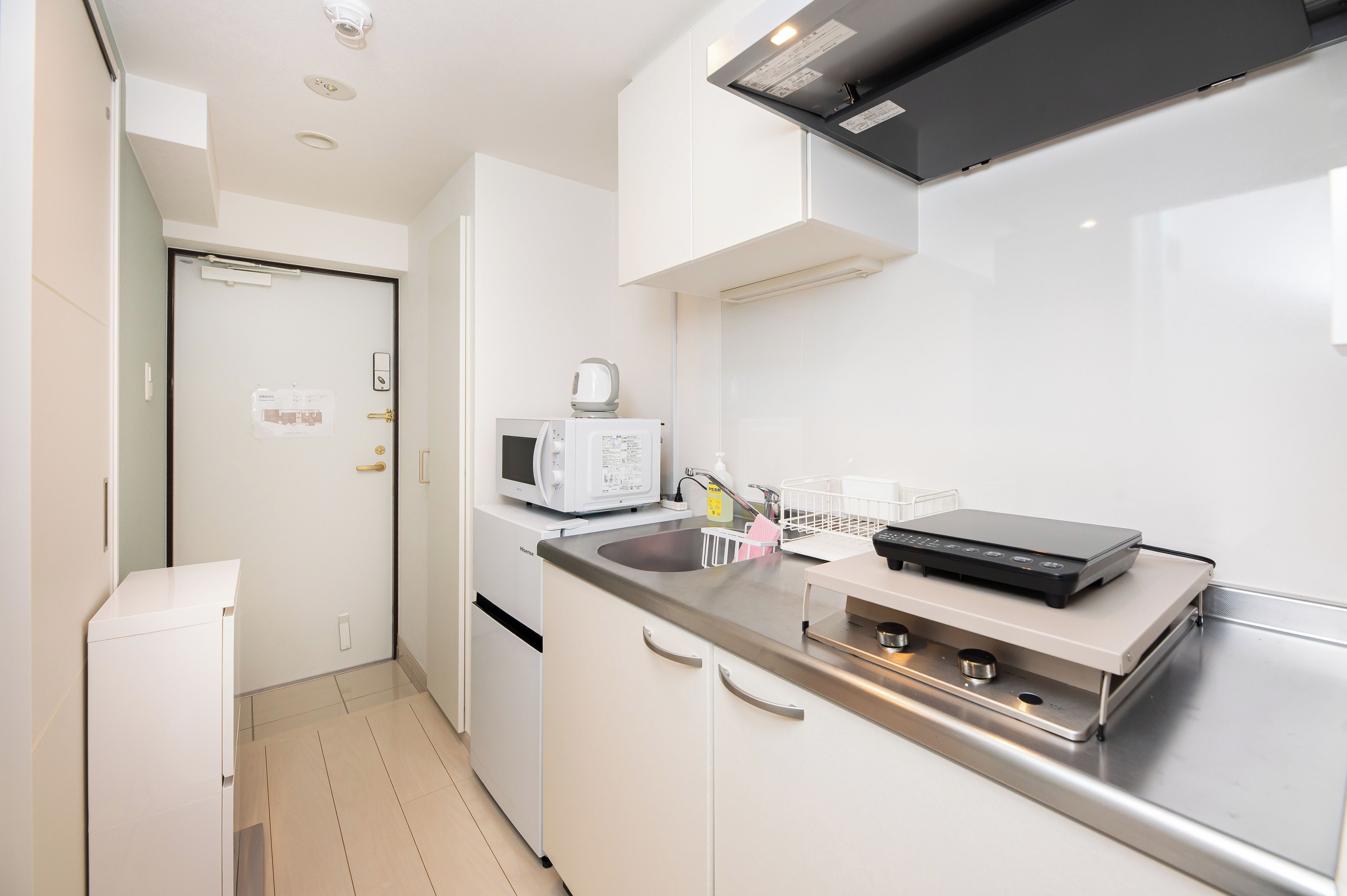 A compact kitchen with white cabinets, a microwave, a kettle, and a coffee maker.