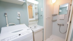 A modern bathroom with a white wash and dry machine, a sink, and a shower area. - Shrine Side Kego Forest (Fukuoka City Chuoku Kego)