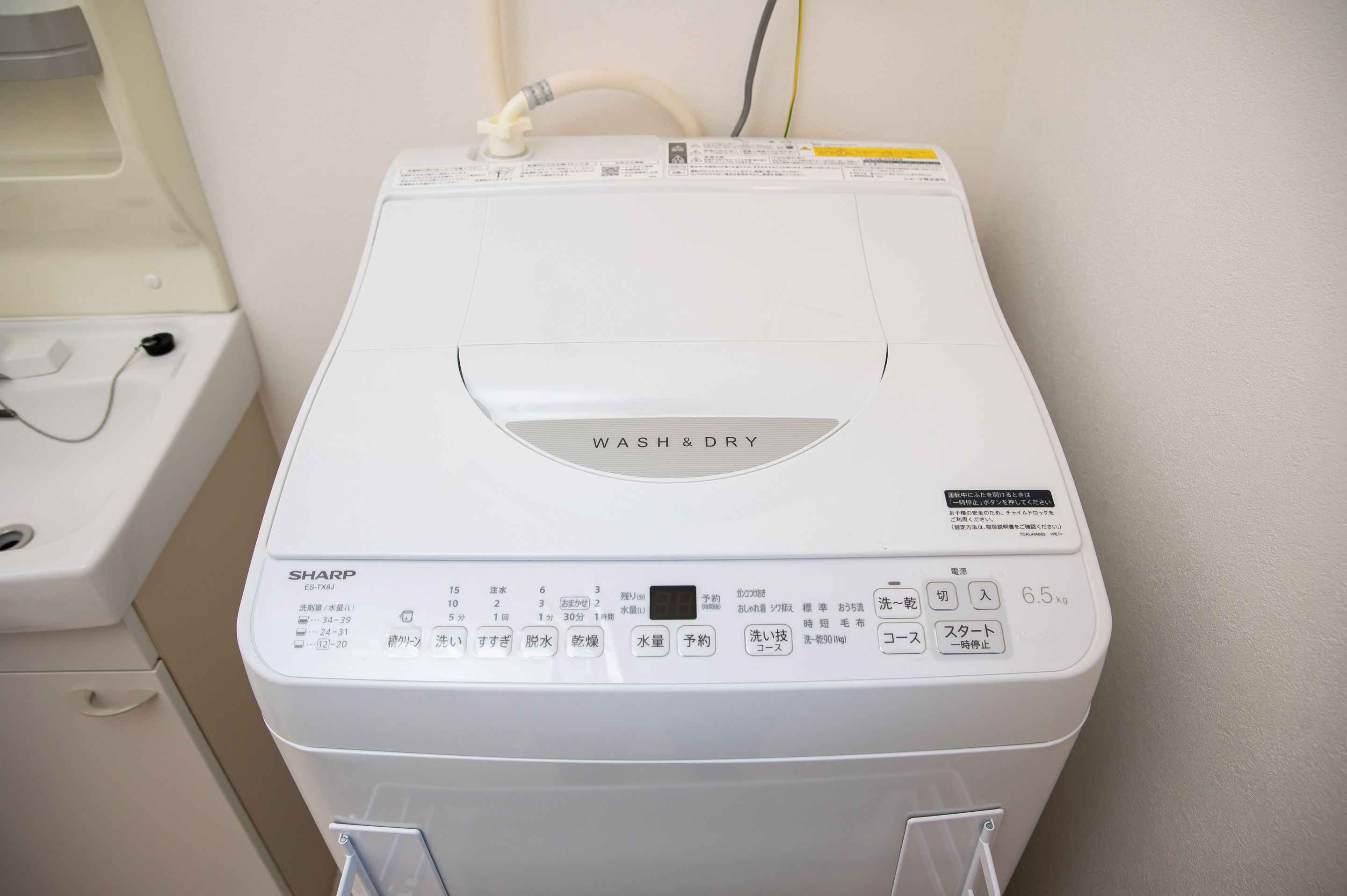 A white front-loading washing machine with a control panel, a water inlet hose, and a drain hose.