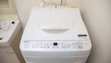 A white front-loading washing machine with a control panel, a water inlet hose, and a drain hose.