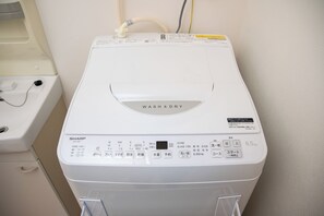 Una lavadora de carga frontal blanca con panel de control, una manguera de entrada de agua y una manguera de desagüe.