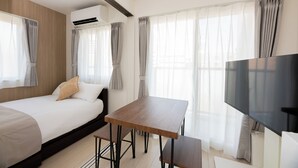 A modern hotel room with a bed, a wooden table, a TV, and large windows with curtains. - Shrine Side Kego Forest (Fukuoka City Chuoku Kego)