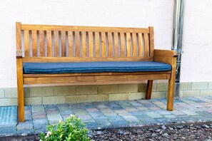 A wooden bench with a blue cushion against a white wall, placed on a stone-paved area. - Holiday apartment in Königheim with barbecue (Königheim)