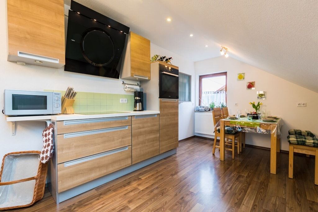 A modern kitchen with a microwave, stove, and wooden cabinets. There is a dining area with a table and chairs.