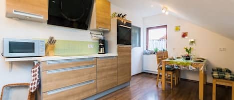 A modern kitchen with a microwave, stove, and wooden cabinets. There is a dining area with a table and chairs.