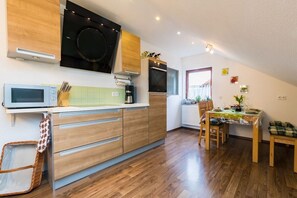 A modern kitchen with a microwave, stove, and wooden cabinets. There is a dining area with a table and chairs. - Holiday apartment in Königheim with barbecue (Königheim)