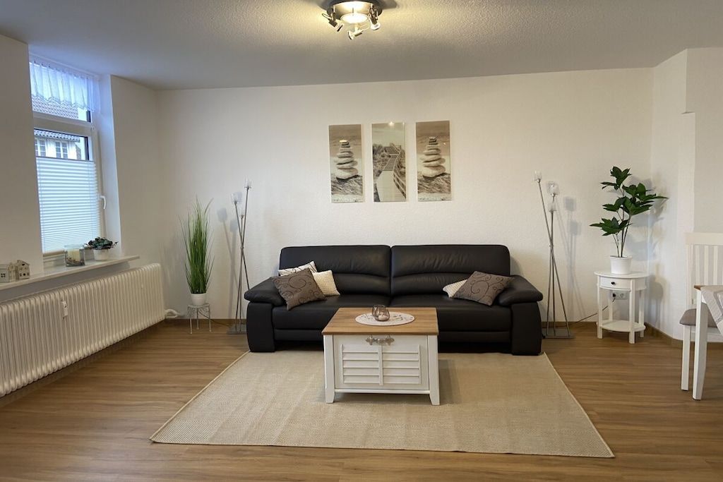 Ein Wohnzimmer mit einem schwarzen Sofa, einem weißen Couchtisch und drei Bildern an der Wand.