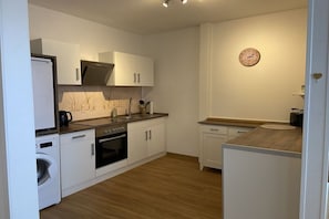 A compact kitchen with white cabinetry, a built-in oven, a washing machine, and a microwave. - Holiday apartment with 1 bedroom (Südheide\/ Hermannsburg)