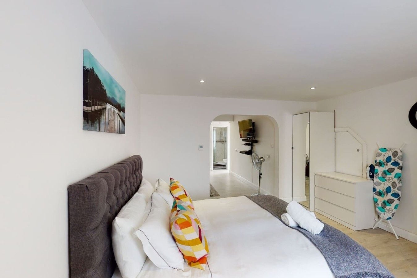 A bedroom with a bed, a dresser, a mirror, and a painting on the wall.