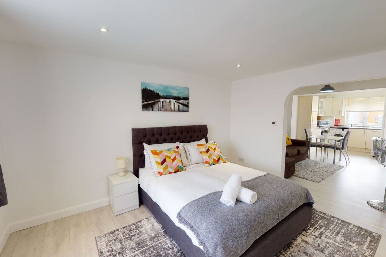 A modern bedroom with a large bed, a bedside table, and a view of the dining area.
