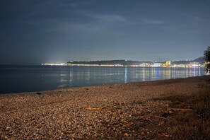 Une plage de galets, une mer calme et, au loin, le paysage urbain.