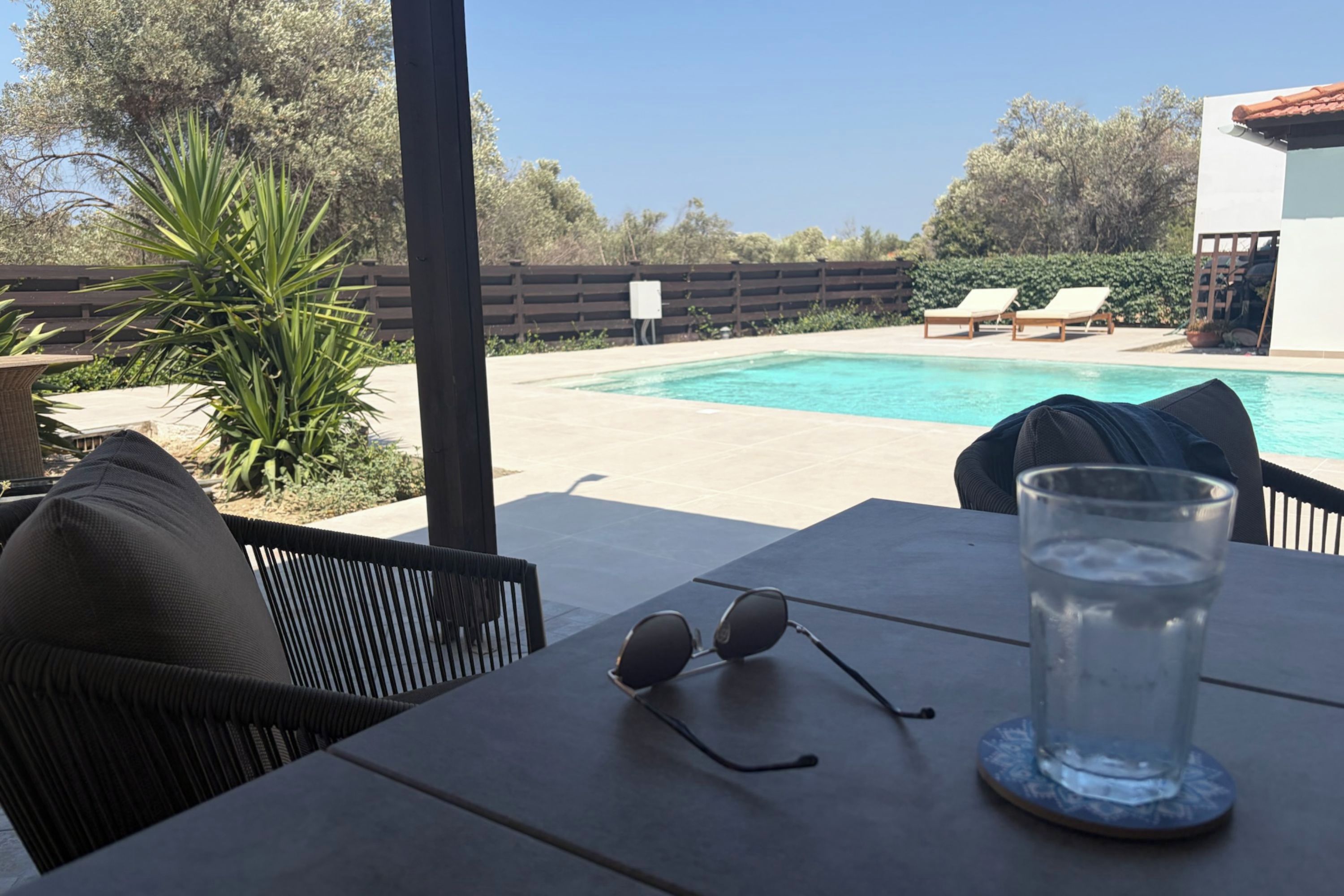 Udsigt over poolen med et bord, stole og et glas vand.