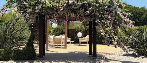 Katettu ulkotila, jossa on pergola, tuoleja ja pyöreä pöytä.