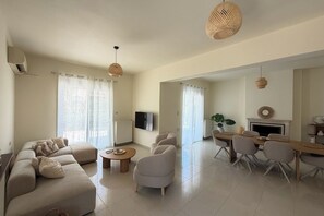 A spacious living room with a sofa, chairs, a coffee table, and a dining area with a table and chairs. - Villa Yasmina (Ialisos)