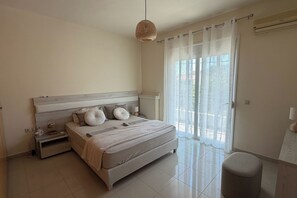 Une chambre à coucher comprenant un lit, des tables de chevet, une lampe, un luminaire suspendu et une fenêtre avec des rideaux.