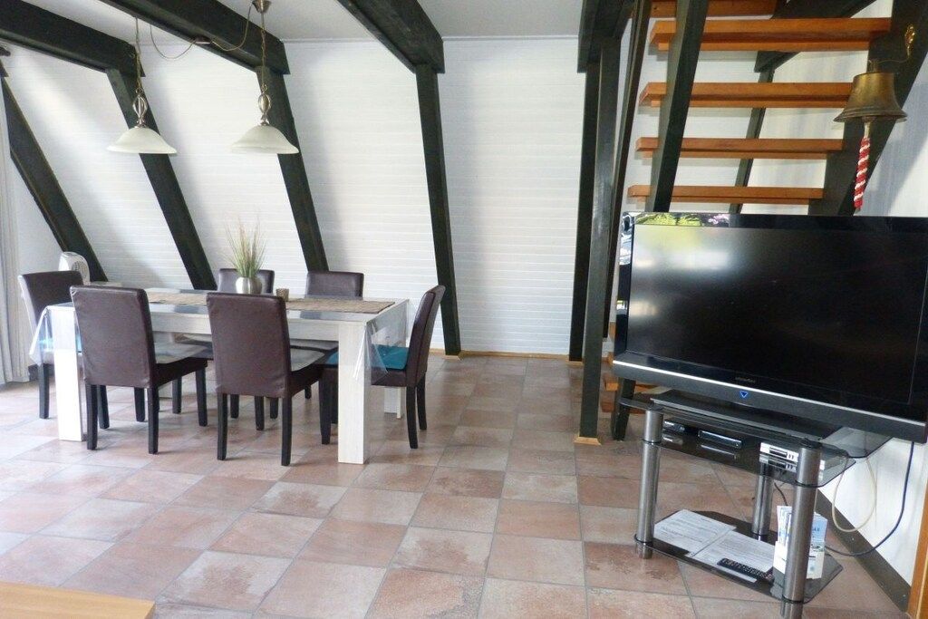 A dining area with a table and chairs, a flat-screen TV on a stand, and a staircase with wooden railings.