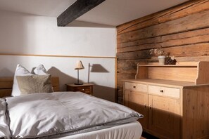 Ein Schlafzimmer mit einem hölzernen Kopfteil, einem Nachttisch mit Lampe, einer Holzkommode und einem Regal mit Dekorationen.