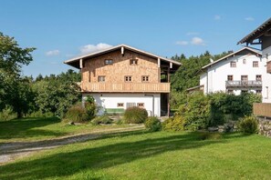 Ein zweistöckiges Gebäude mit Holzfassade, einem Balkon im oberen Geschoss und einem umgebenden Garten.