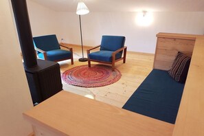 A cozy room with a wooden floor, two blue chairs, a small table, a red patterned rug, a wooden cabinet, and a black heater. - Holiday home with 1 bedroom (Rattenberg)