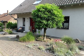 A residential house with a tiled roof, a red door, and a well-maintained garden with various plants and flowers. - Holiday apartment with 1 bedroom (Trierweiler)