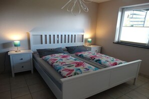 Een slaapkamer met een wit bed, twee nachtkastjes en een raam.